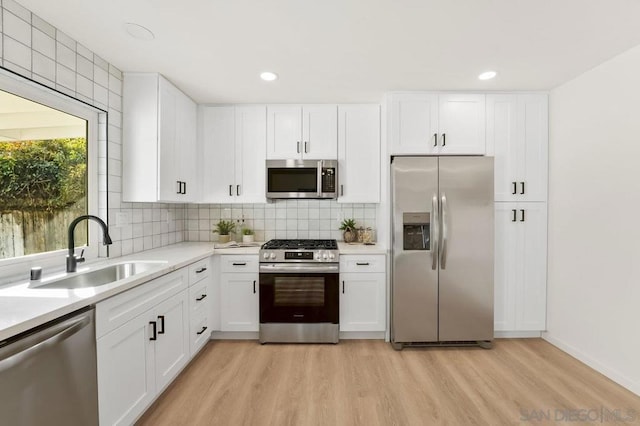 kitchen with stainless steel appliances, sink, white cabinets, and light wood-type flooring