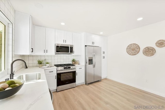 kitchen featuring sink, appliances with stainless steel finishes, white cabinetry, light stone counters, and light wood-type flooring