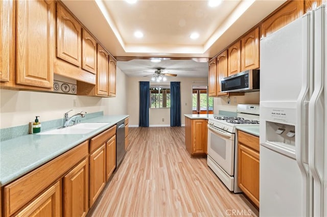 kitchen with a raised ceiling, sink, ceiling fan, stainless steel appliances, and light wood-type flooring