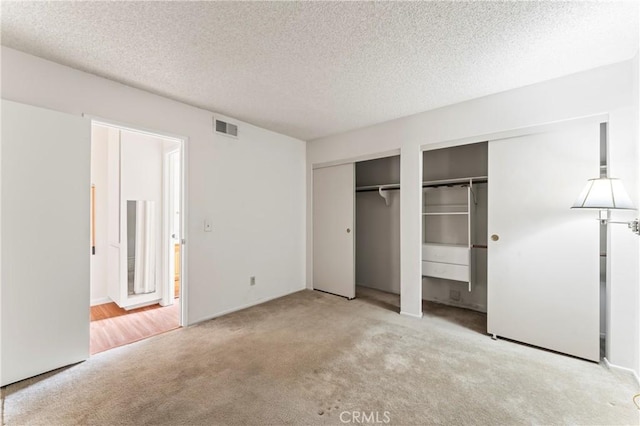 unfurnished bedroom featuring multiple closets, light carpet, and a textured ceiling