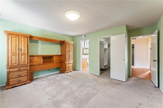 unfurnished bedroom featuring connected bathroom, a spacious closet, a textured ceiling, a closet, and light colored carpet