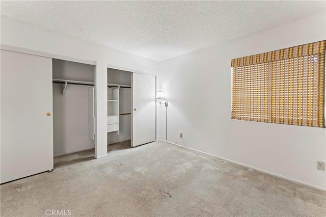 unfurnished bedroom with carpet floors, a textured ceiling, and two closets