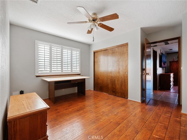 bedroom with dark wood-type flooring, a textured ceiling, ceiling fan, and a closet