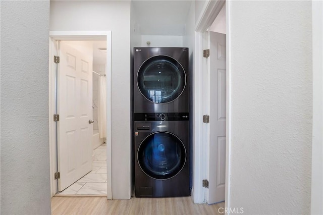 laundry area with light wood-type flooring, stacked washer and clothes dryer, a textured wall, and laundry area