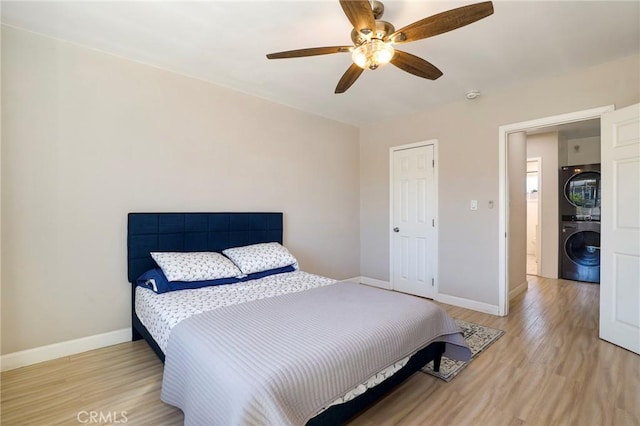 bedroom with light wood-style floors, stacked washer / drying machine, baseboards, and a ceiling fan