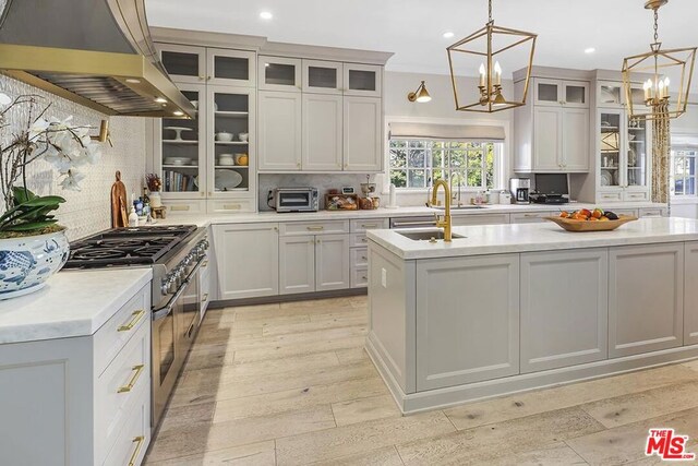 kitchen featuring high end stainless steel range, a chandelier, an island with sink, pendant lighting, and island exhaust hood