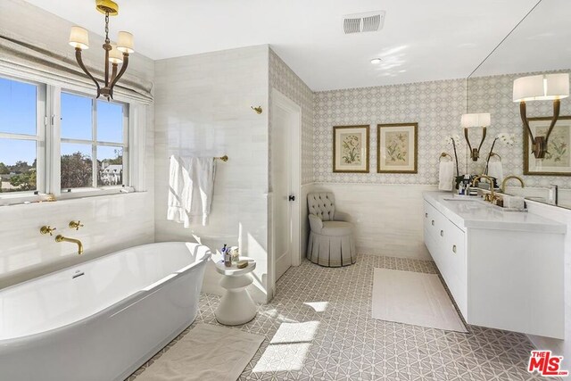 bathroom featuring tile patterned floors, an inviting chandelier, tile walls, vanity, and a bathing tub