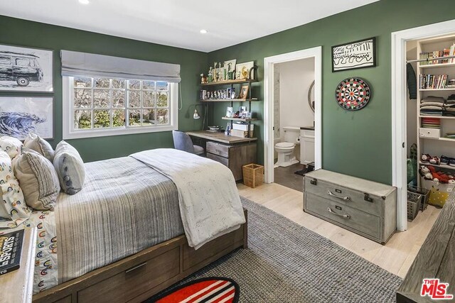 bedroom with a closet, a spacious closet, ensuite bathroom, and light wood-type flooring