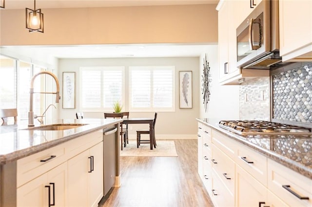 kitchen with sink, white cabinetry, hanging light fixtures, appliances with stainless steel finishes, and light stone countertops