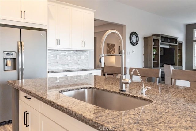 kitchen with white cabinetry, sink, decorative backsplash, stainless steel fridge with ice dispenser, and light stone countertops