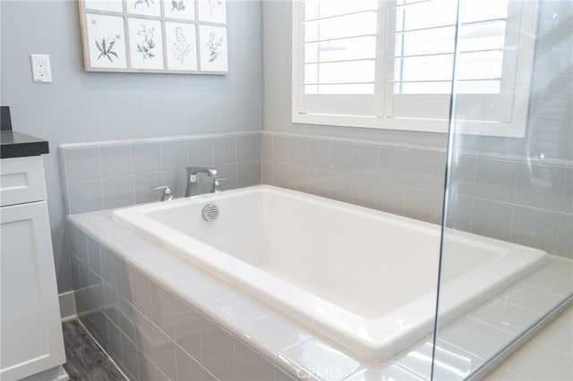 bathroom with a relaxing tiled tub, vanity, and a wealth of natural light