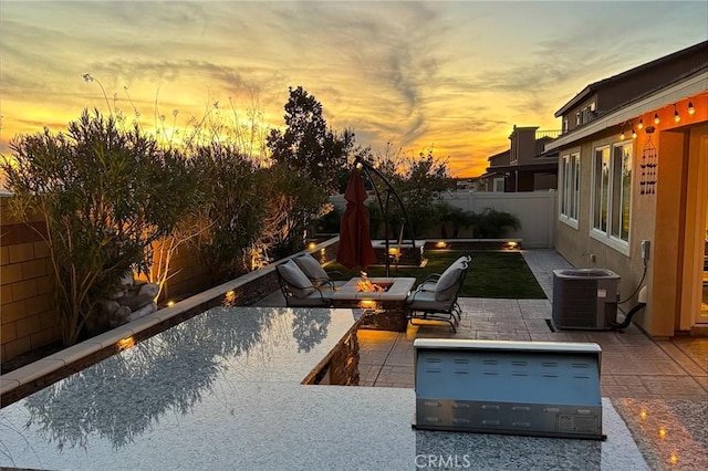 patio terrace at dusk featuring cooling unit and a fire pit