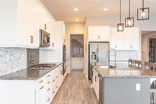 kitchen featuring appliances with stainless steel finishes, a breakfast bar, pendant lighting, white cabinetry, and an island with sink