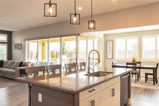 kitchen featuring sink, white cabinets, hanging light fixtures, light stone counters, and a center island with sink