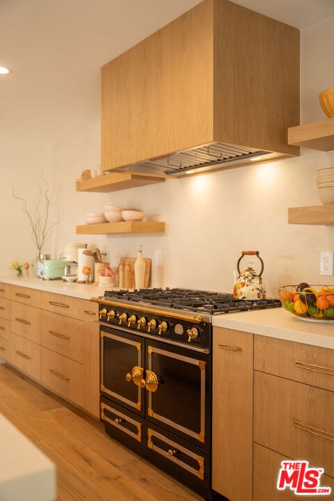 kitchen with light brown cabinetry, custom range hood, range with two ovens, and light wood-type flooring