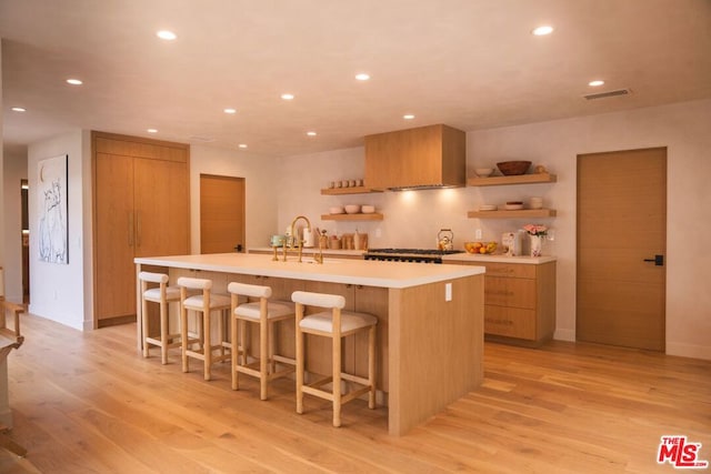 kitchen featuring a kitchen breakfast bar, a kitchen island with sink, sink, and light hardwood / wood-style floors