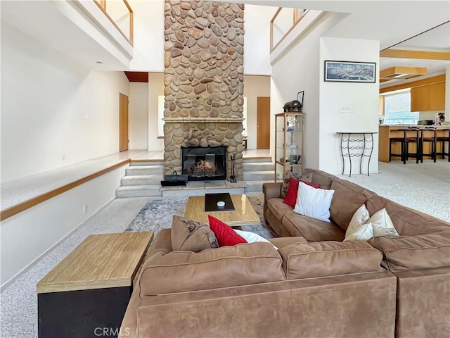 living room with light carpet, a stone fireplace, and a high ceiling