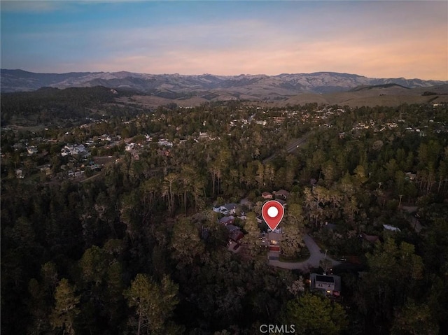 aerial view at dusk featuring a mountain view and a wooded view