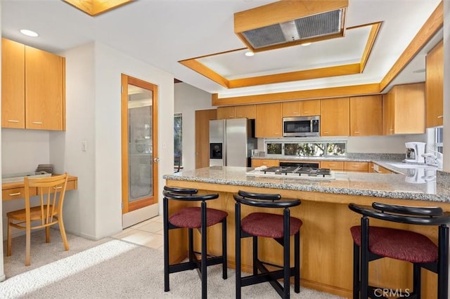 kitchen with a peninsula, appliances with stainless steel finishes, a kitchen breakfast bar, and a raised ceiling