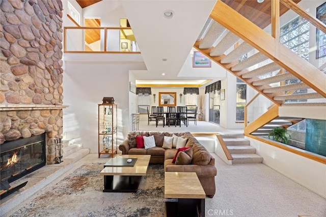 living area featuring stairs, a stone fireplace, and a high ceiling