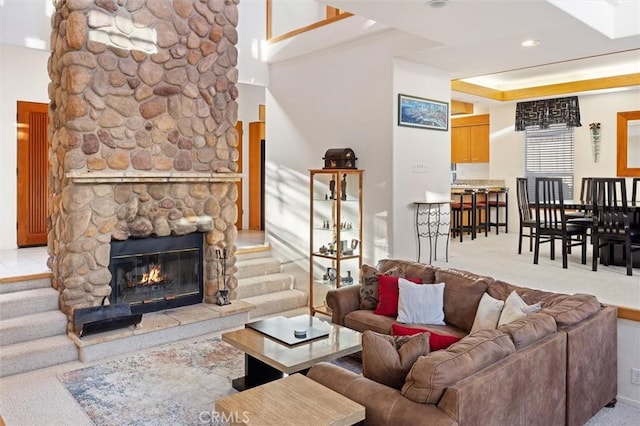 living area with a raised ceiling, light carpet, and a stone fireplace