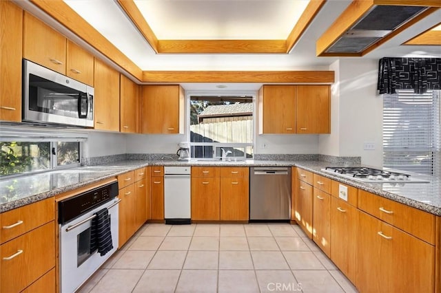 kitchen featuring brown cabinetry, extractor fan, a tray ceiling, and stainless steel appliances