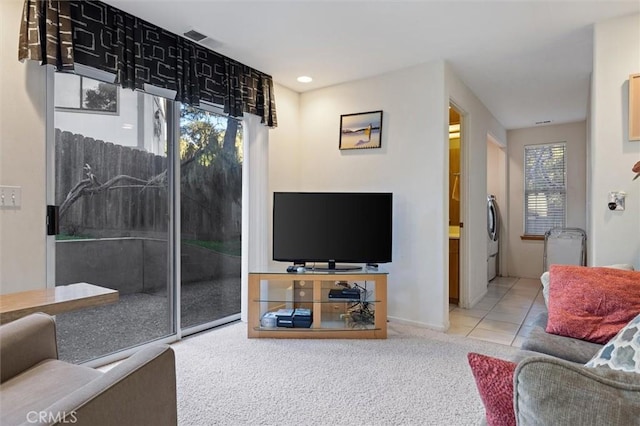 living area with washer / clothes dryer, light colored carpet, and light tile patterned floors