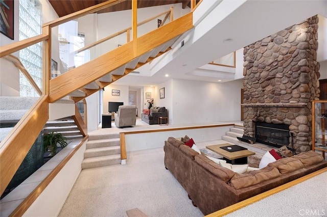 living room with carpet floors, a stone fireplace, stairway, and a towering ceiling