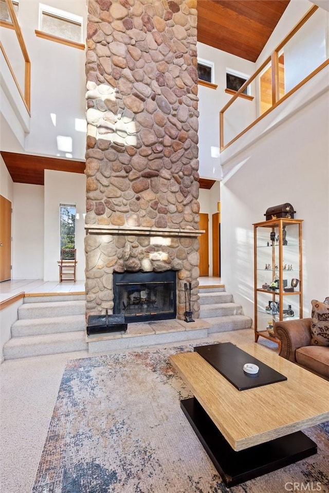 living area with stairs, a stone fireplace, wooden ceiling, and a towering ceiling