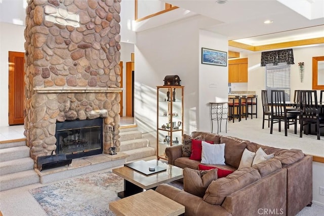 living area with a tray ceiling, a stone fireplace, stairway, and light colored carpet