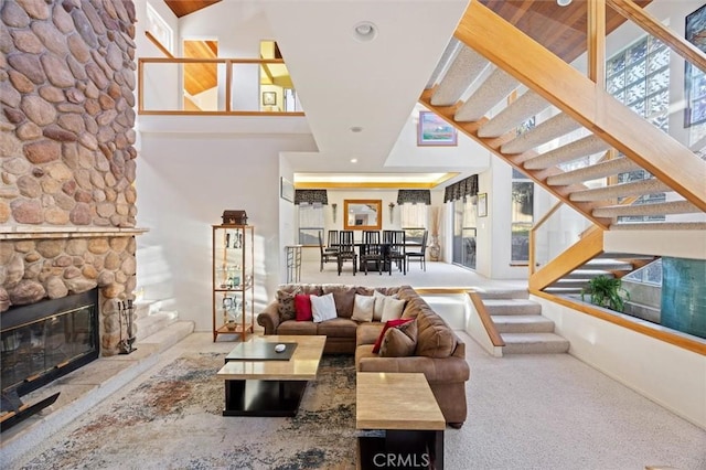 living area featuring stairway, a stone fireplace, and a towering ceiling