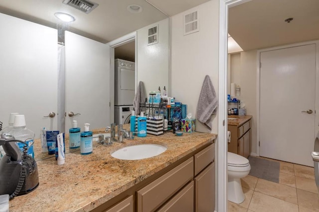 bathroom featuring vanity, stacked washer / drying machine, tile patterned floors, and toilet