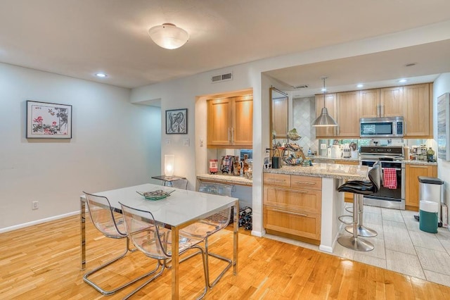 kitchen with tasteful backsplash, a kitchen breakfast bar, stove, light stone countertops, and light wood-type flooring