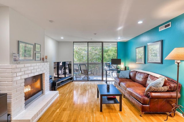 living room with a brick fireplace, a wall of windows, and light wood-type flooring