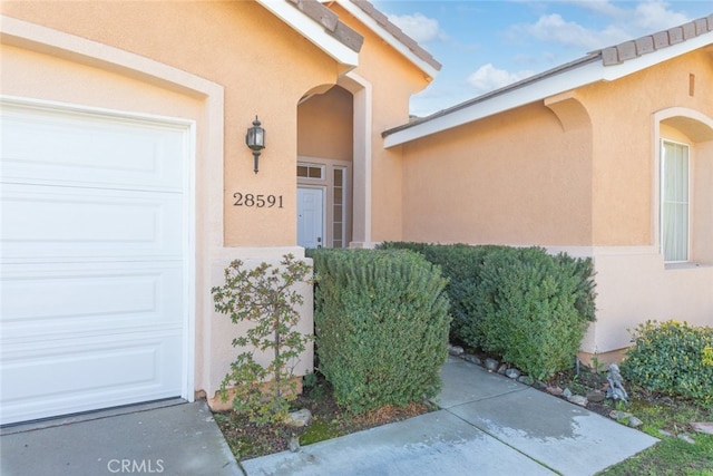 view of exterior entry featuring a garage and stucco siding