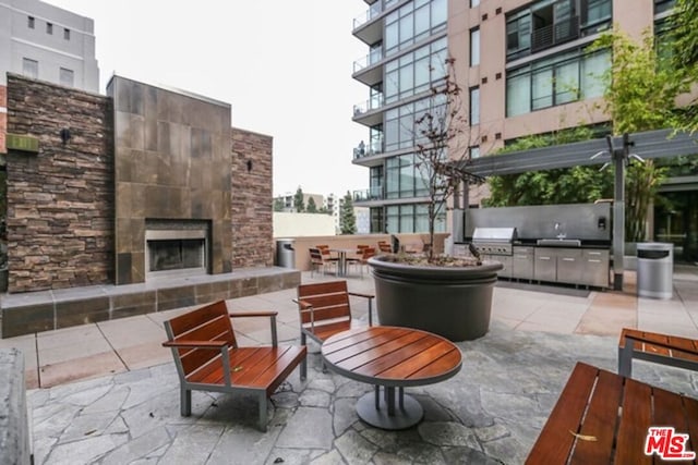 view of patio / terrace with a grill, a pergola, an outdoor stone fireplace, and exterior kitchen