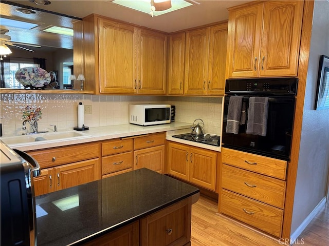 kitchen featuring sink, tasteful backsplash, light wood-type flooring, ceiling fan, and black appliances