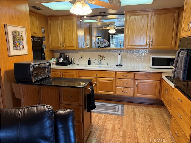 kitchen featuring sink, ceiling fan, tasteful backsplash, black fridge, and light wood-type flooring