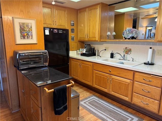 kitchen featuring tasteful backsplash, sink, ceiling fan, black fridge, and light hardwood / wood-style flooring