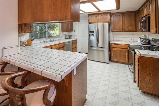 kitchen featuring appliances with stainless steel finishes, tile countertops, a kitchen breakfast bar, and kitchen peninsula