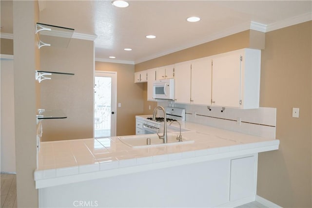 kitchen with ornamental molding, tile counters, kitchen peninsula, white appliances, and white cabinets