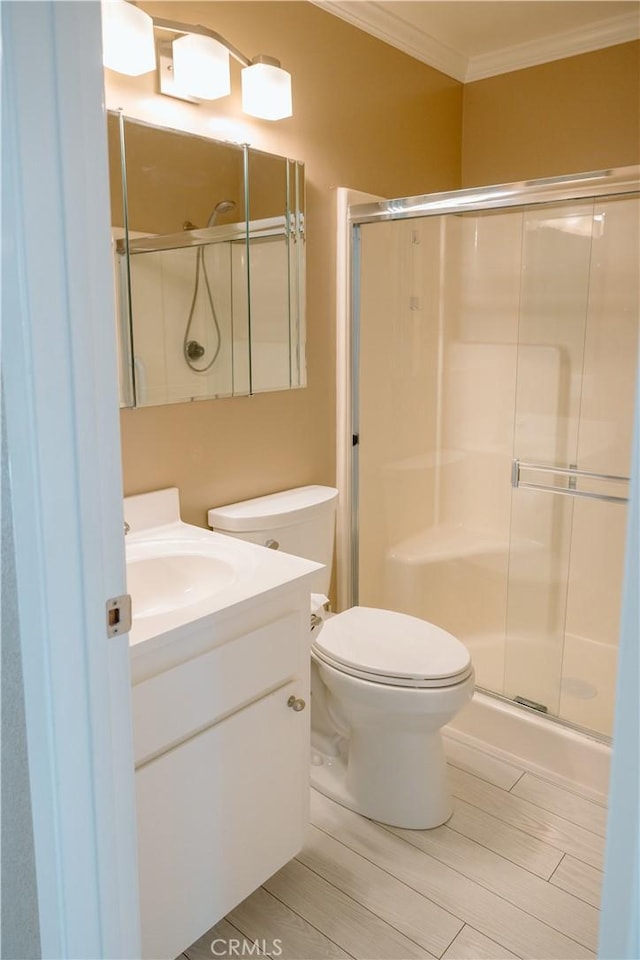 bathroom with a shower with door, vanity, crown molding, and toilet