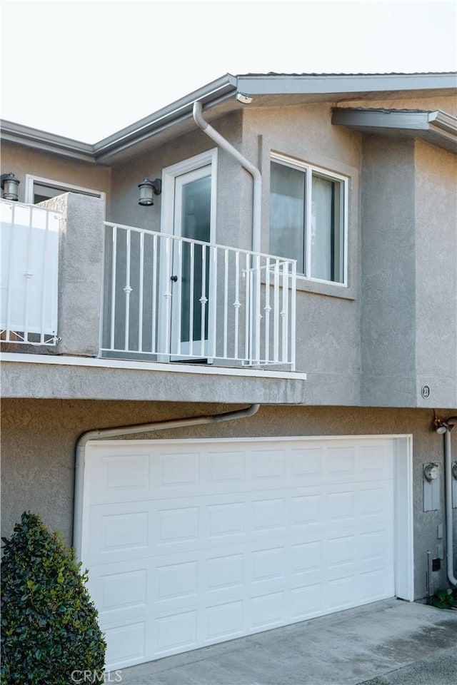view of side of home featuring stucco siding, an attached garage, concrete driveway, and a balcony