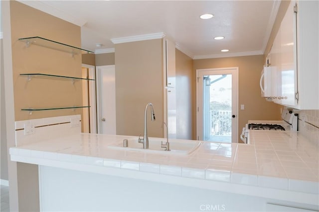 kitchen with tile countertops, sink, white cabinets, crown molding, and white appliances