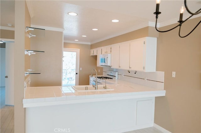 kitchen featuring a peninsula, ornamental molding, a sink, and white appliances