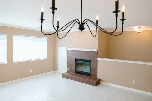 unfurnished living room featuring wood finished floors, ornamental molding, baseboards, a chandelier, and a tiled fireplace