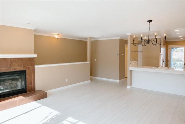 unfurnished living room with a sink, a chandelier, a tiled fireplace, baseboards, and ornamental molding
