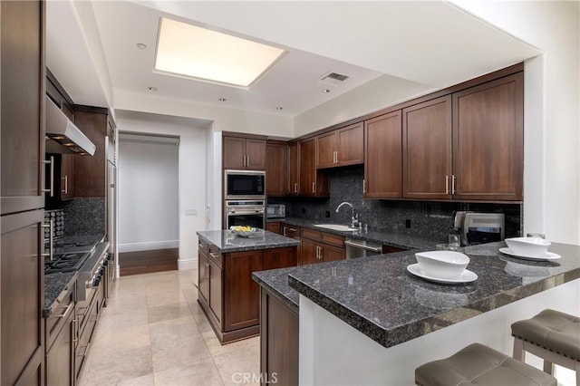 kitchen featuring dark brown cabinetry, sink, dark stone countertops, a kitchen island, and stainless steel appliances