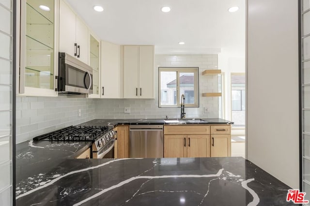 kitchen with sink, appliances with stainless steel finishes, tasteful backsplash, dark stone counters, and light brown cabinets