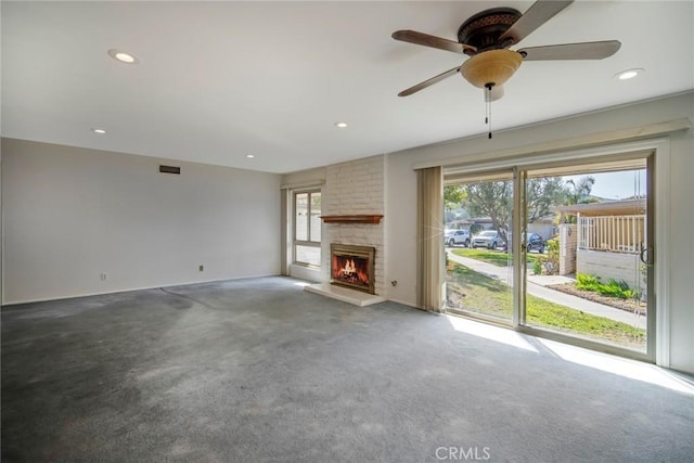 unfurnished living room featuring a stone fireplace, ceiling fan, and carpet